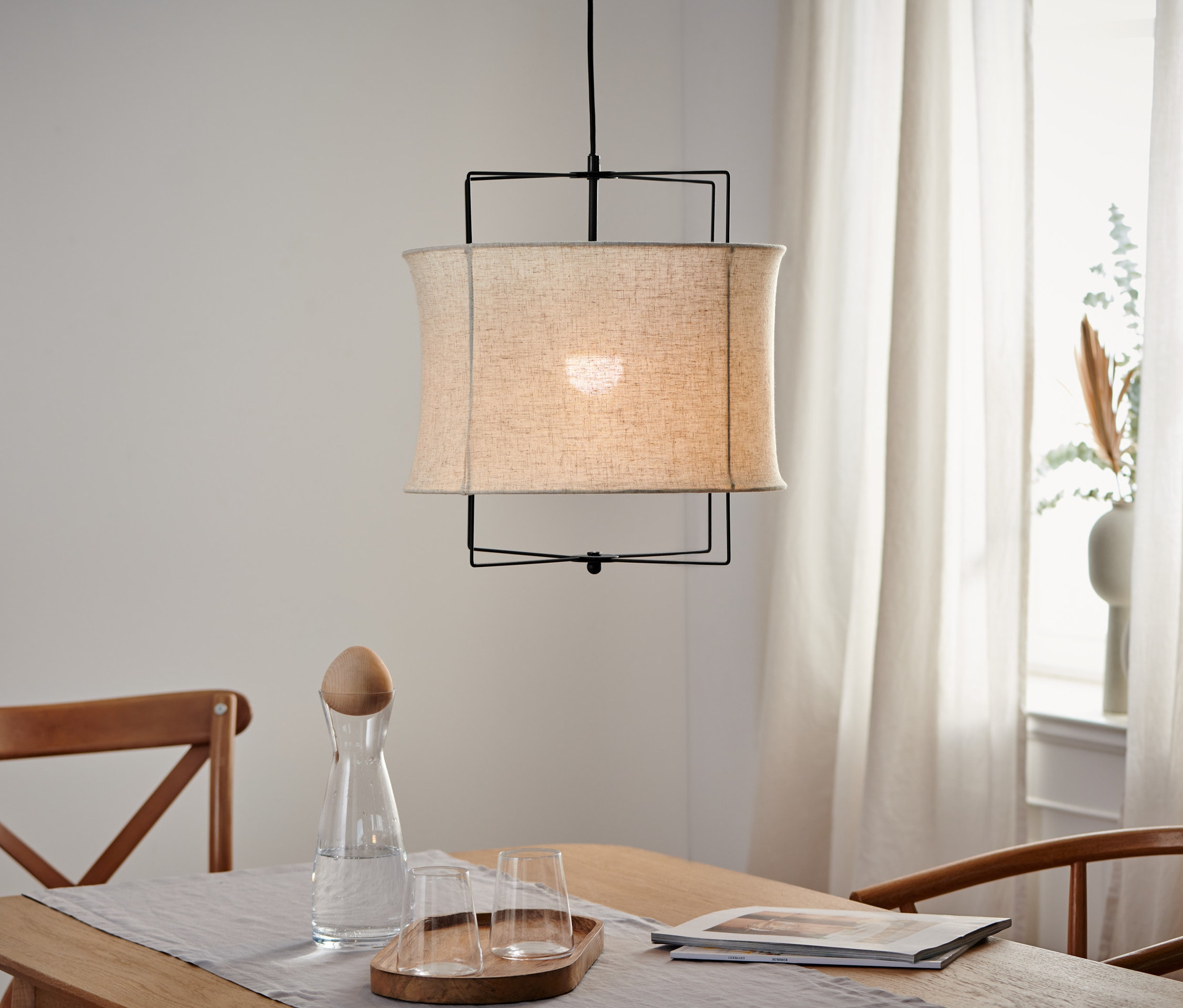 Lampa wisząca z kloszem z tkaniny wisi nad drewnianym stołem.