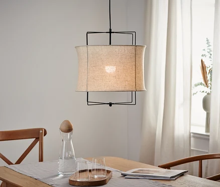 Lampa wisząca z kloszem z tkaniny wisi nad drewnianym stołem.