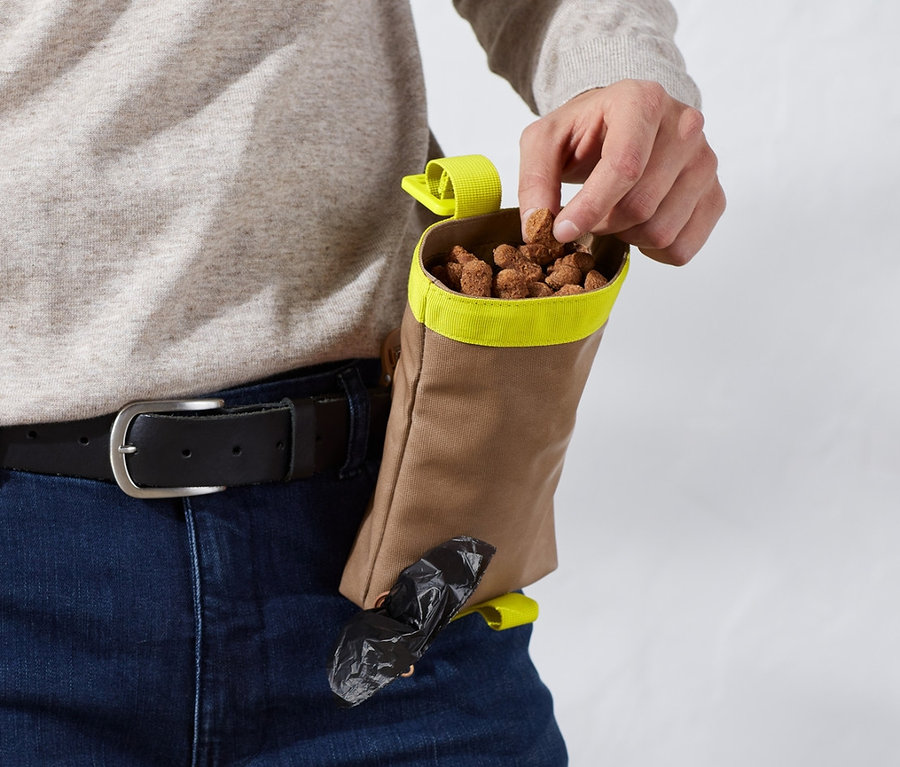 Mężczyzna wyjmuje smakołyk z saszetki na spacery z psem.