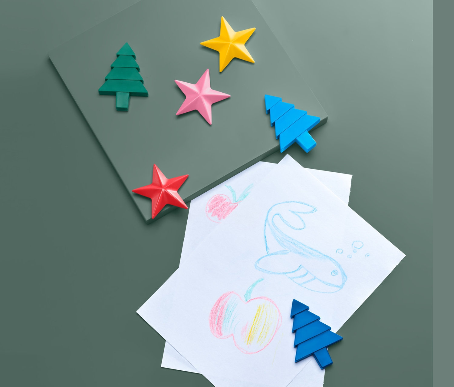 Dziecięce rysunki i kredki woskowe, 6 sztuk, na zielonym tle.