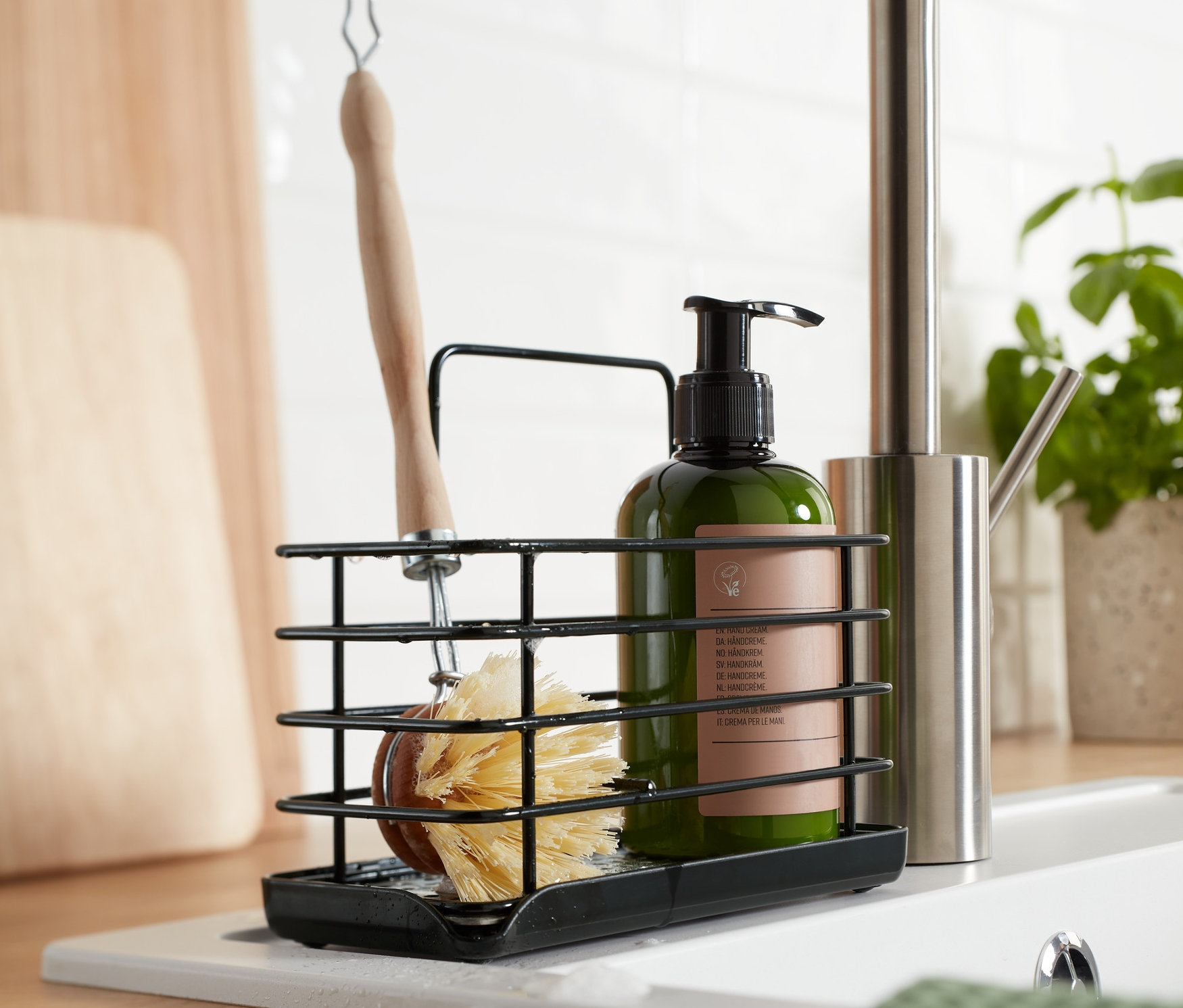 Czarny, metalowy stojak na przybory do zmywania ze szczotką i butelką mydła na zlewie.