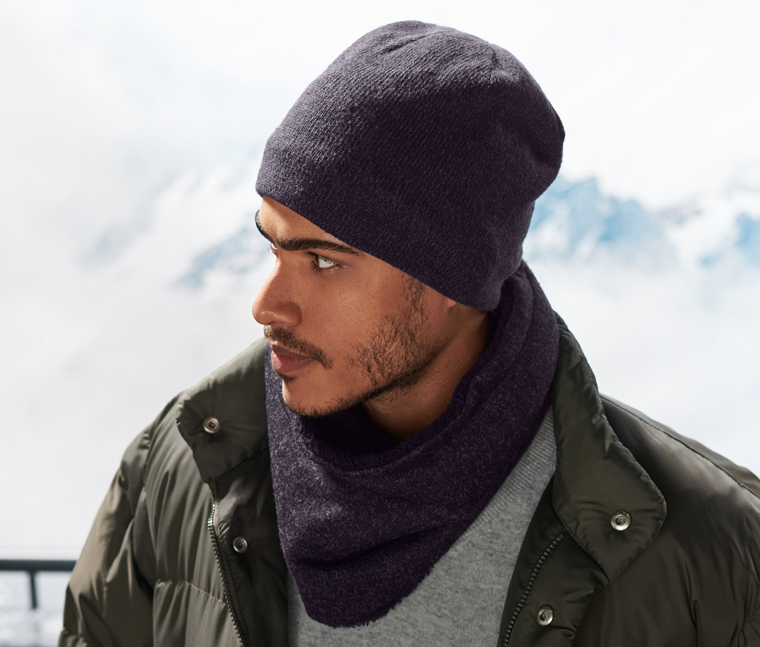 Mężczyzna w niebieskim szaliku z dzianiny polarowej i czapce, w tle ośnieżone góry.