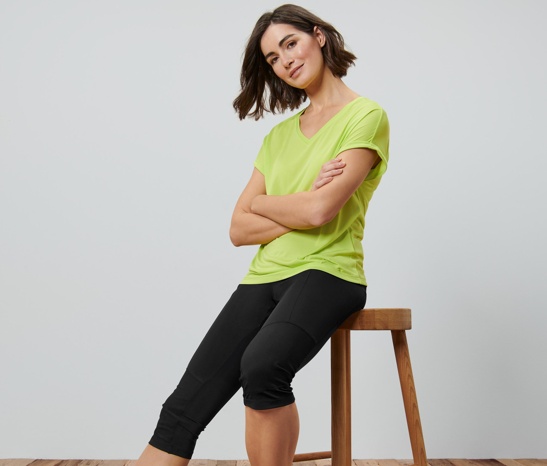 Kobieta siedzi na stołku ze skrzyżowanymi ramionami, ubrana w czarne legginsy trekkingowe o długości 3/4.