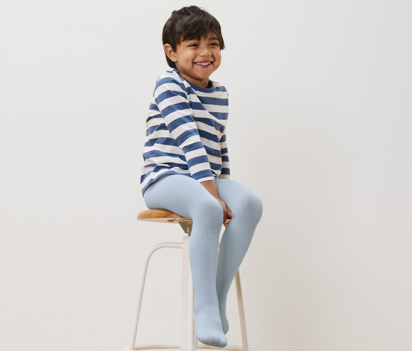 Chłopiec siedzi na stołku i ma na sobie niebieskie bawełniane rajstopy.