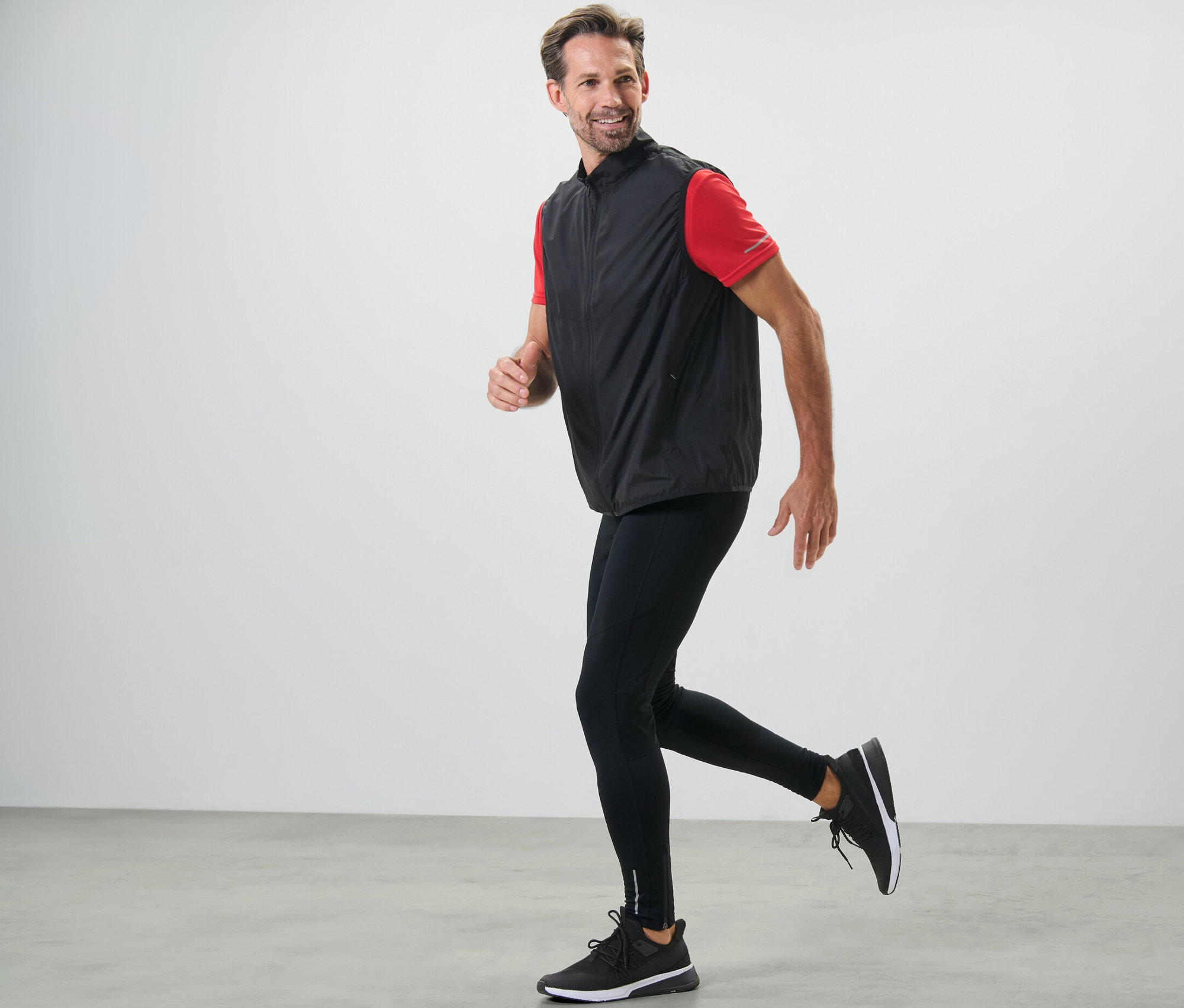 Mężczyzna biegnie w czarnych legginsach do biegania i kamizelce.