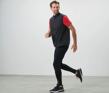 Mężczyzna biegnie w czarnych legginsach do biegania i kamizelce.