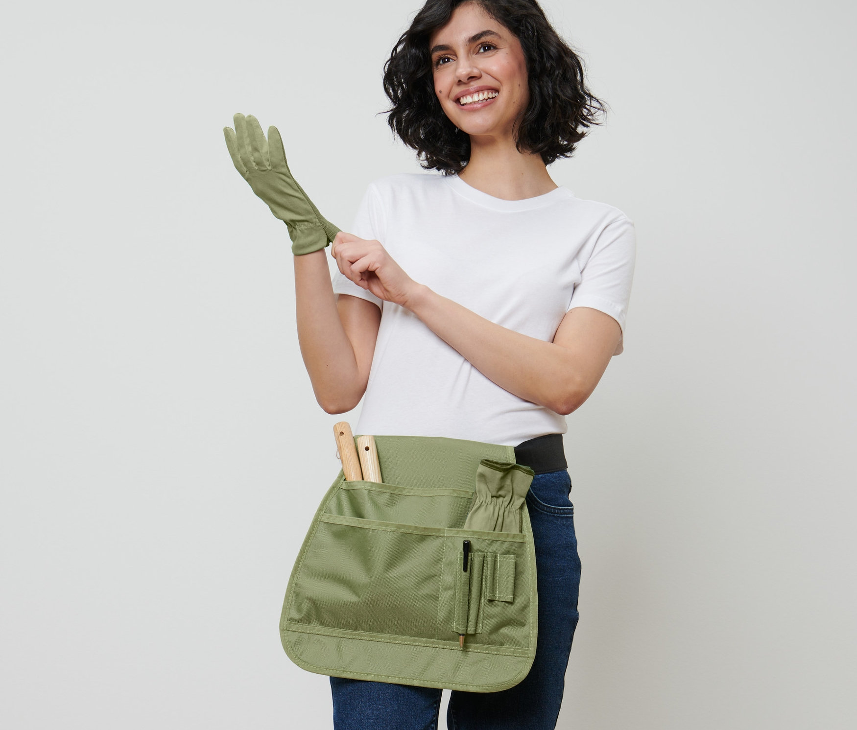 Kobieta zakłada rękawicę ogrodniczą i nosi pas na narzędzia ogrodnicze.