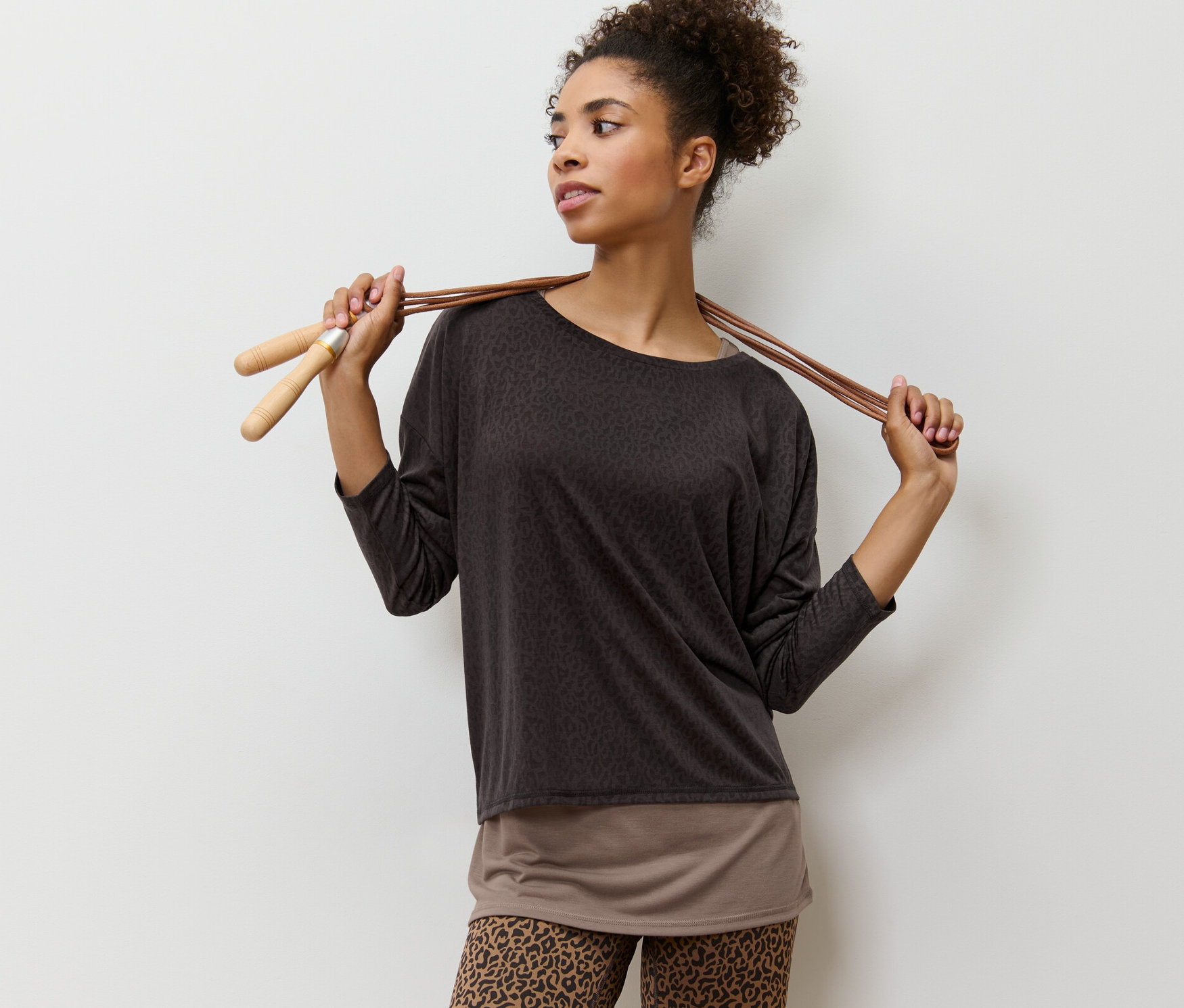 Kobieta pozuje w brązowej koszulce sportowej 2 w 1 i ze skakanką.