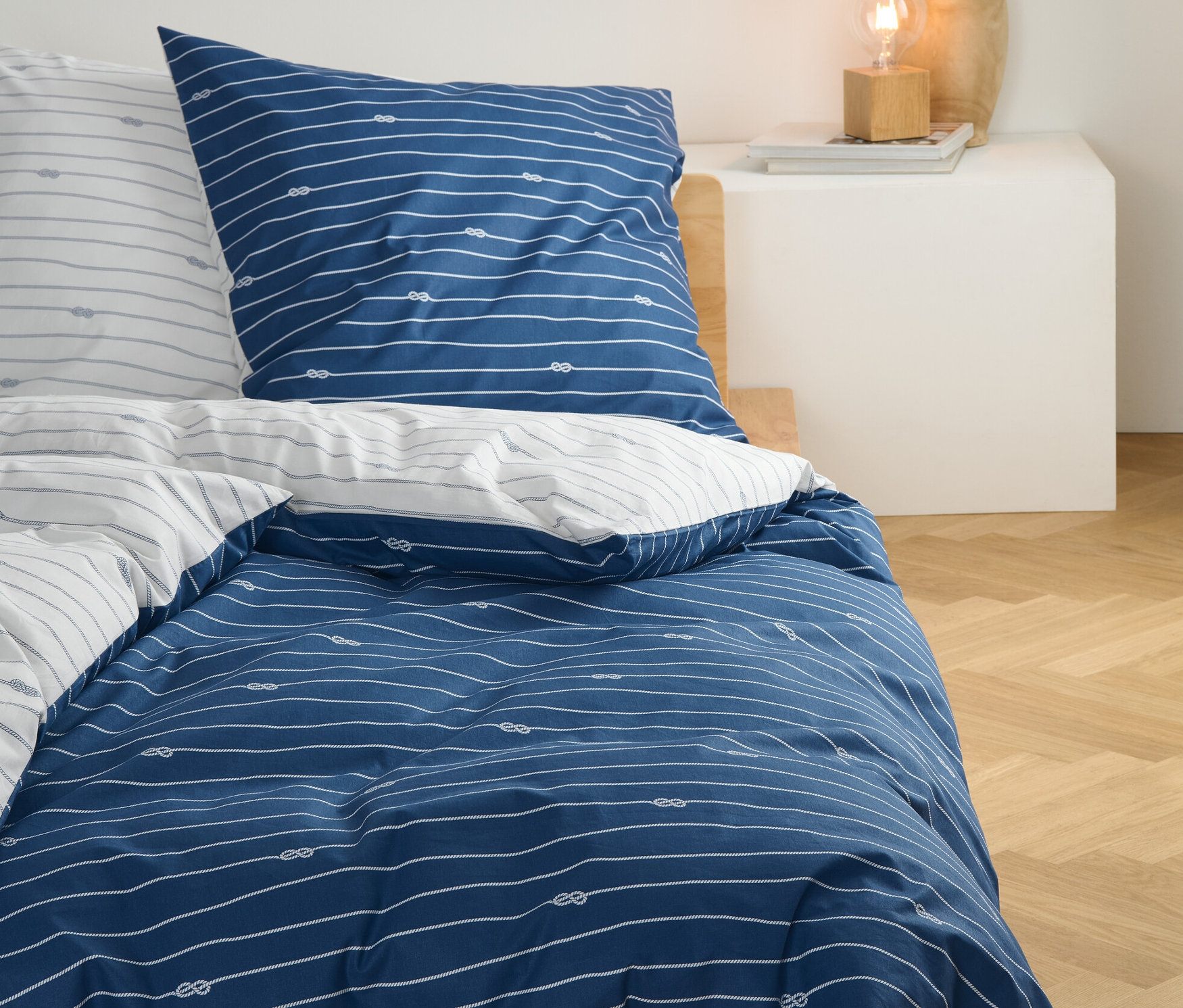 Niebieska pościel perkalowa w standardowym rozmiarze z białymi paskami i wzorem węzłów na łóżku.