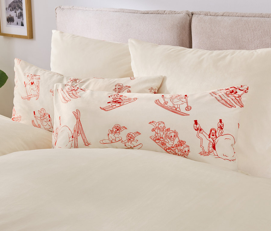 Beżowa pościel z poduszkami z czerwonymi postaciami z kreskówek na nartach i snowboardach.