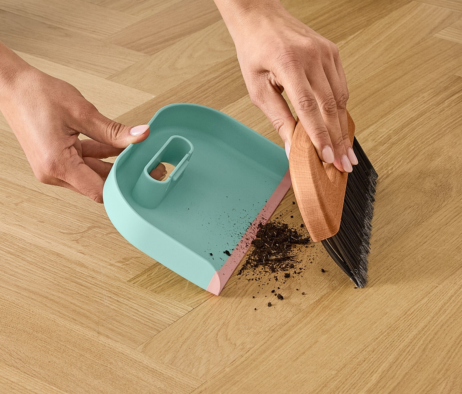 Kobieta zamiata brud zmiotką i szufelką na drewnianej podłodze.