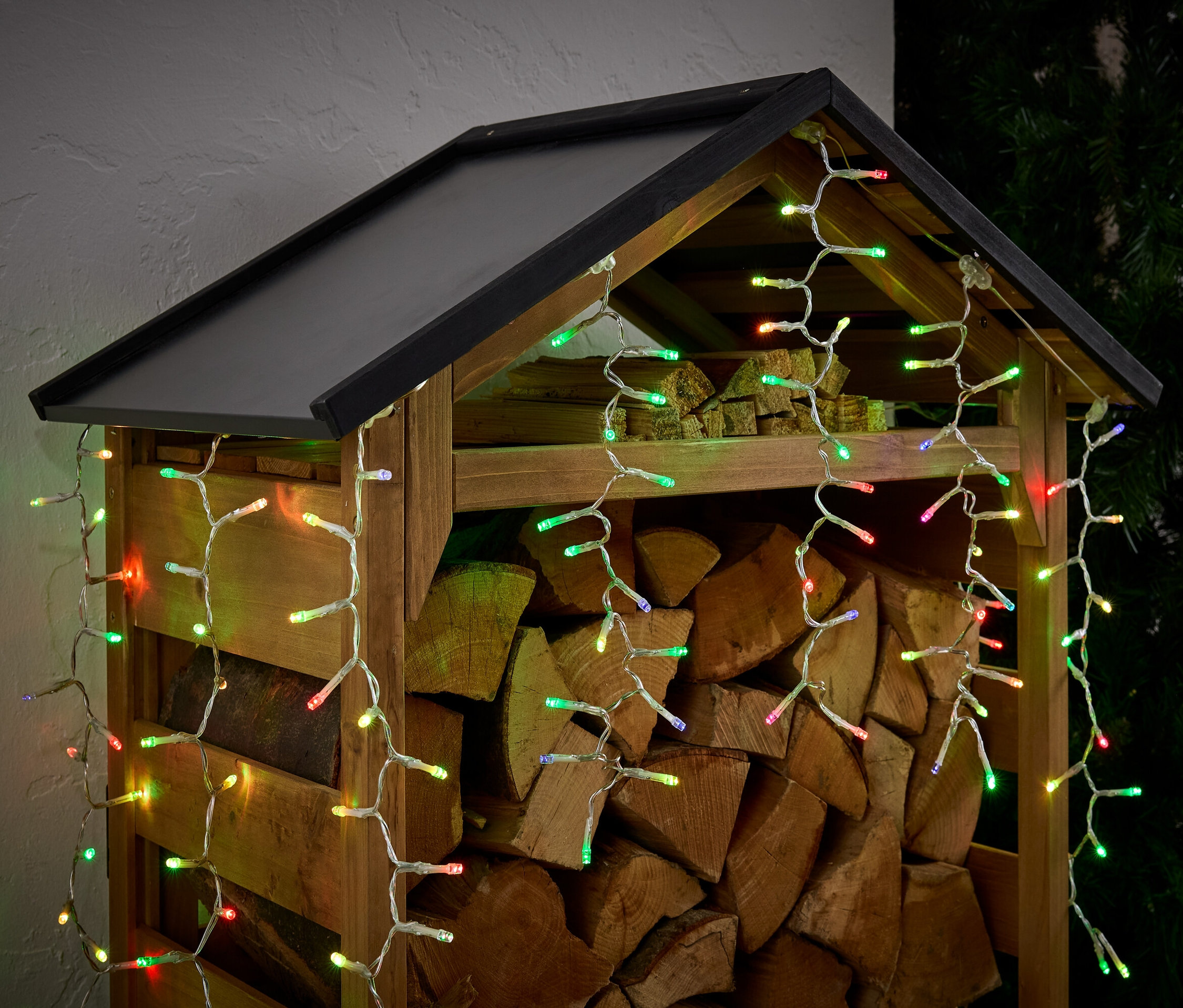 Drewutnia wypełniona drewnem, ozdobiona kolorowymi światełkami.