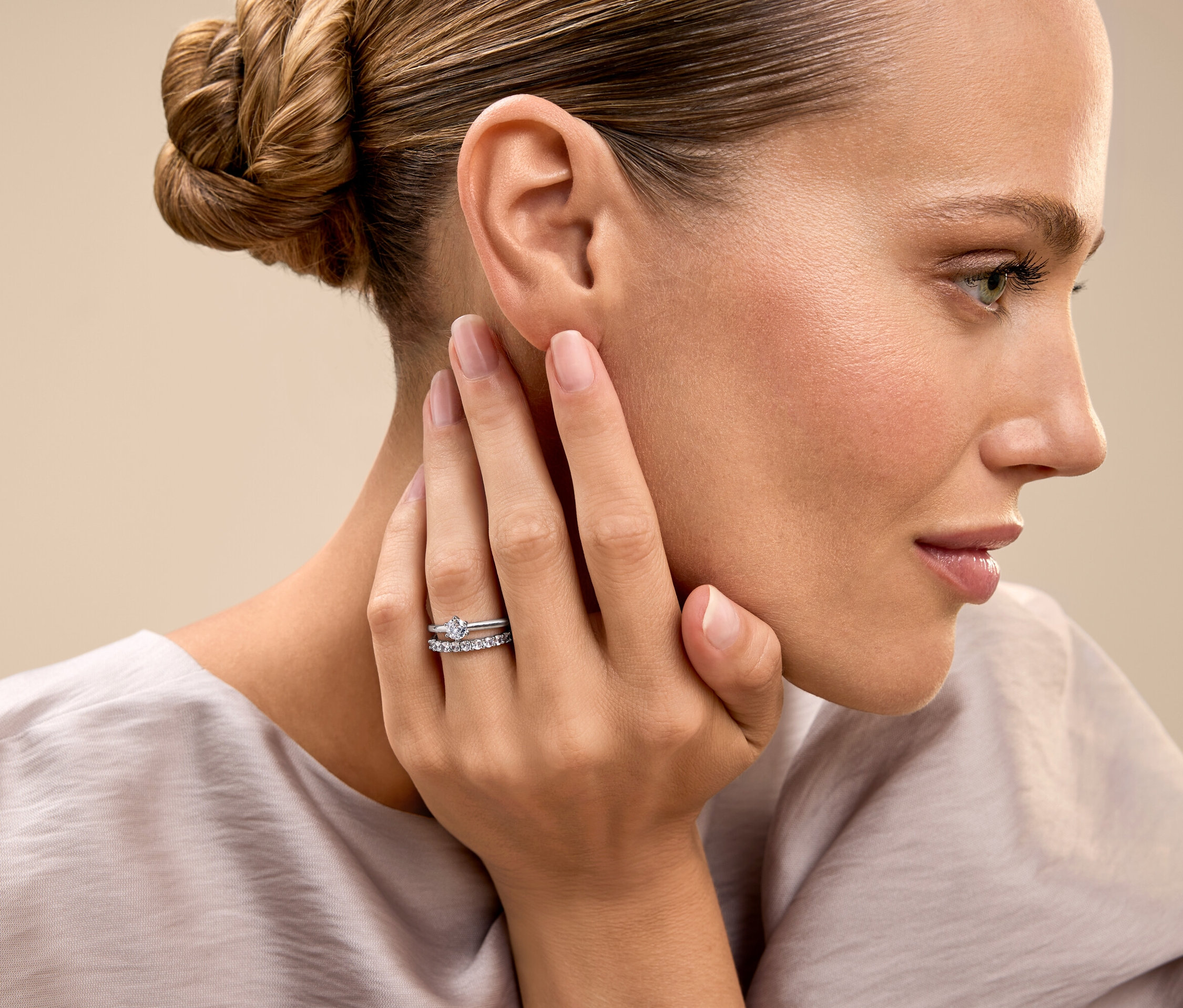 Kobieta z upiętymi włosami dotyka twarzy i pokazuje pierścionek.