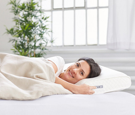 Uśmiechnięta kobieta leży w łóżku na poduszce Medisana Sleep-Well »SP 100«, z dźwiękiem.