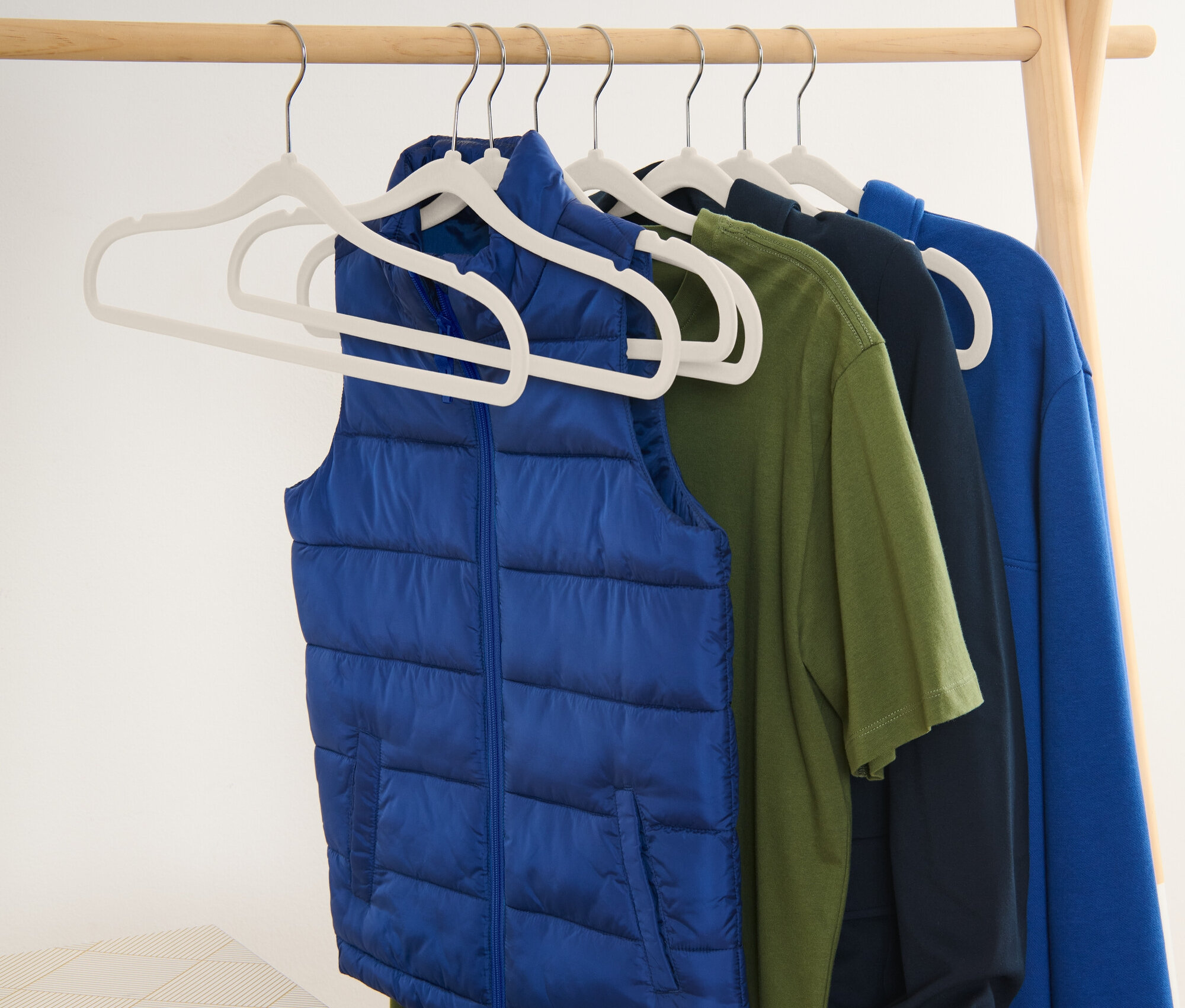 Niebieska kamizelka i koszulki wiszą na wieszakach na drewnianym stojaku.