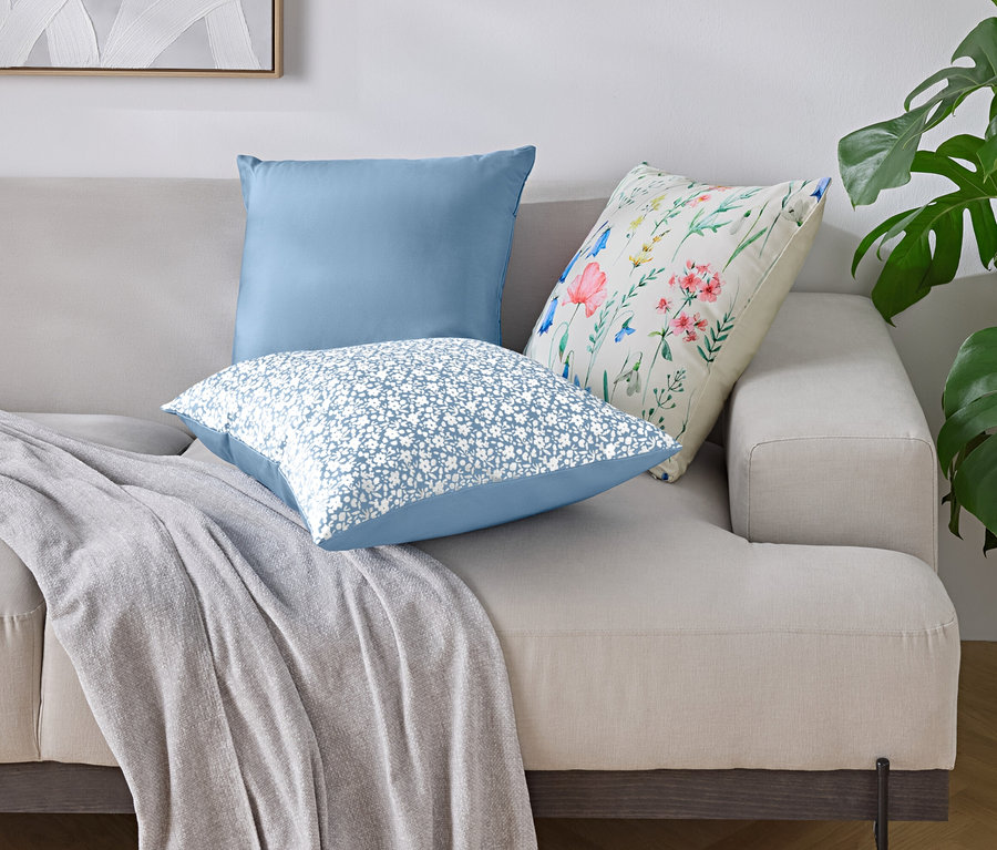 Na sofie leżą trzy poduszki i koc.