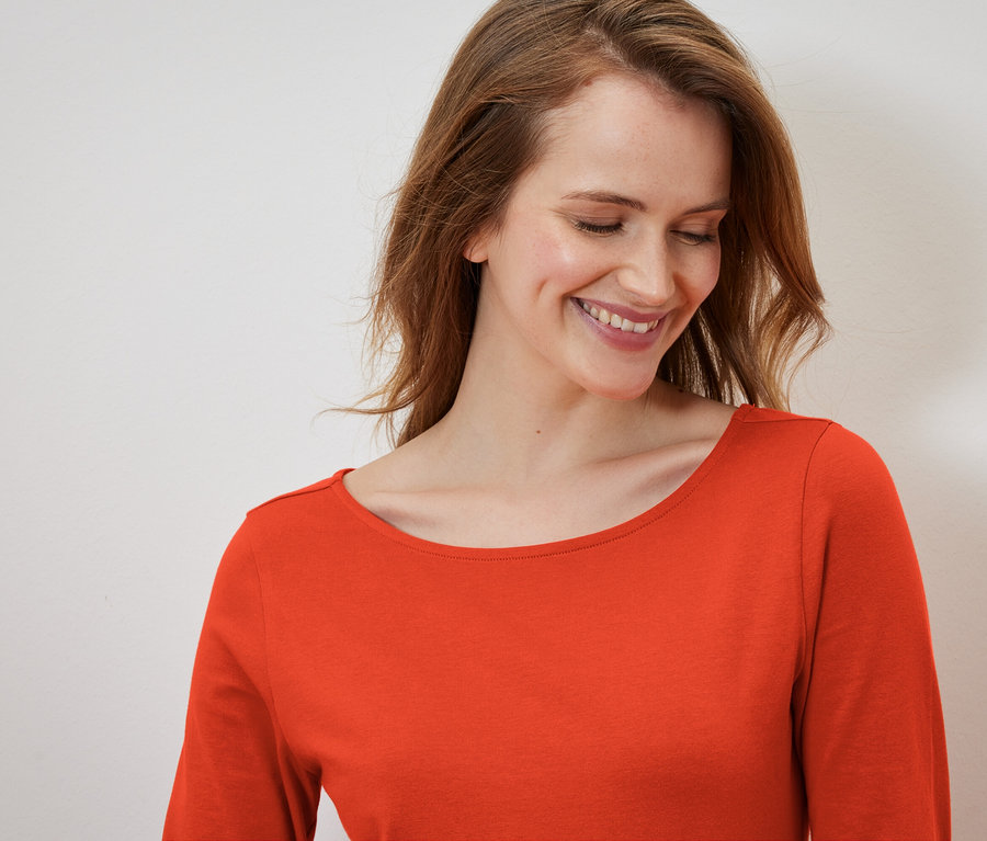 Uśmiechnięta kobieta z długimi włosami w pomarańczowej koszulce z długim rękawem.