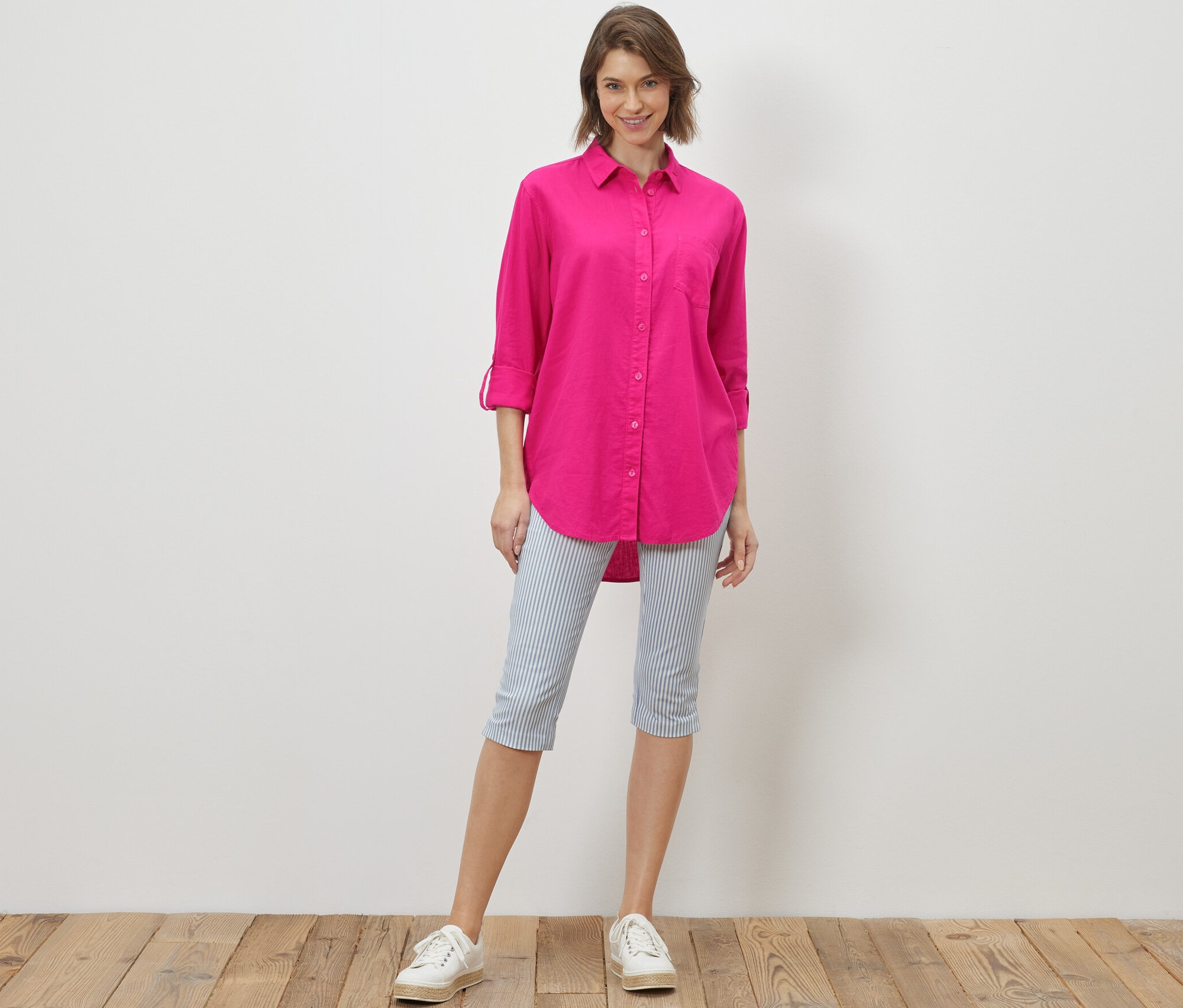Kobieta stoi i ma na sobie długą lnianą bluzkę w kolorze różowym.
