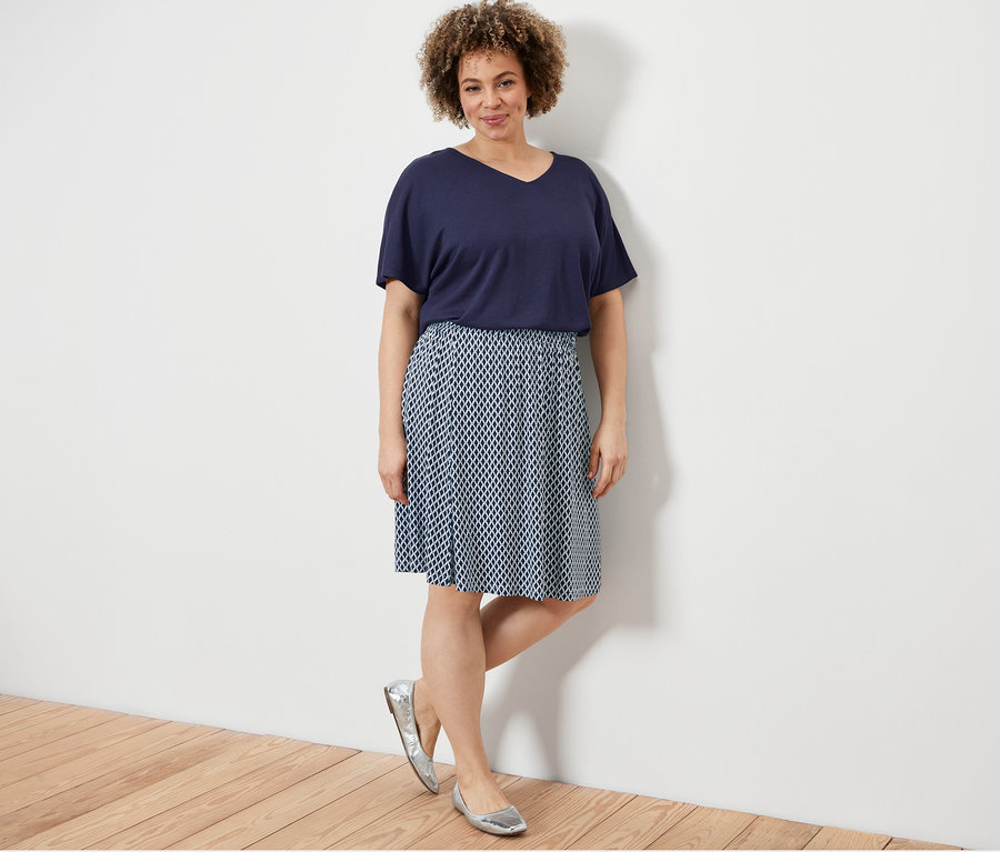 Kobieta pozuje w granatowej koszulce z fakturowaną powierzchnią i spódnicy z dżerseju z nadrukiem.