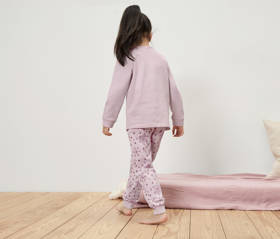 Dziewczynka w piżamie z długim rękawem i płatkami śniegu idzie po drewnianej podłodze.