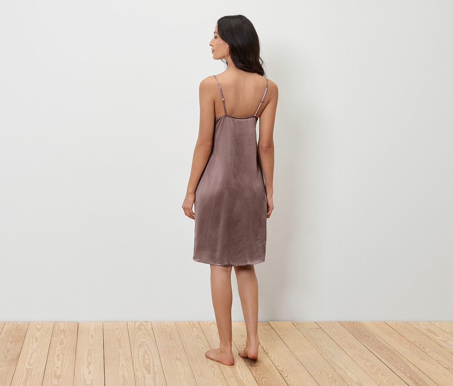 Kobieta stoi tyłem do kamery i ma na sobie fioletową koszulę nocną.