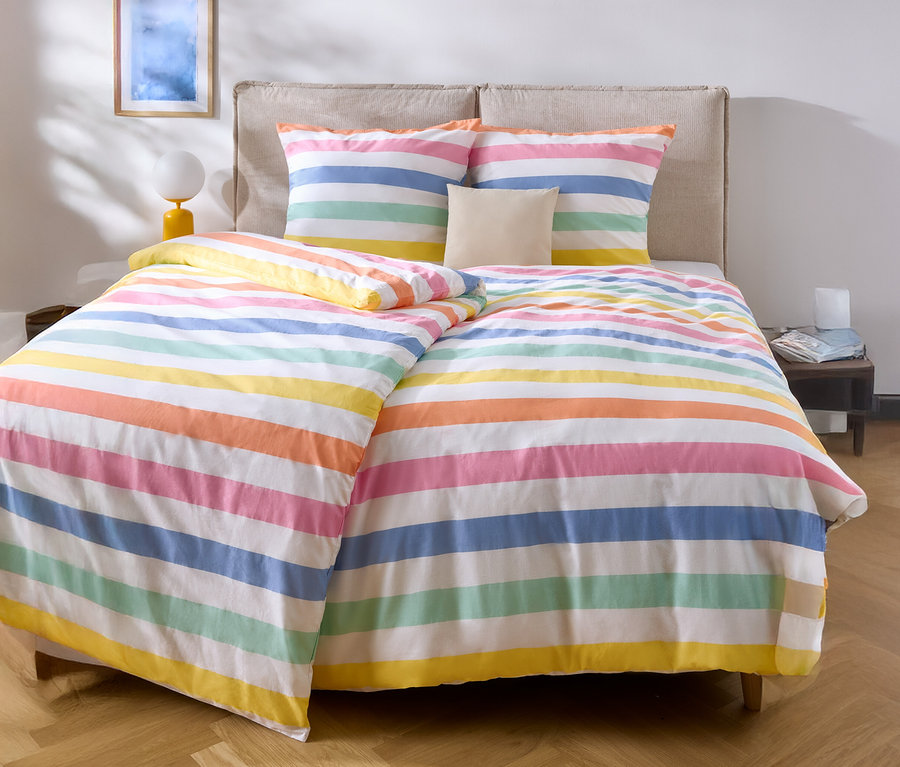 Łóżko z kolorową pościelą w paski i dwiema poduszkami.