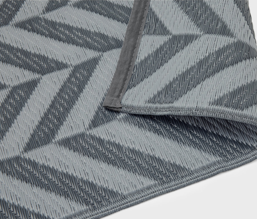 Szara mata piknikowa ze wzorem geometrycznym leży złożona na białym tle.