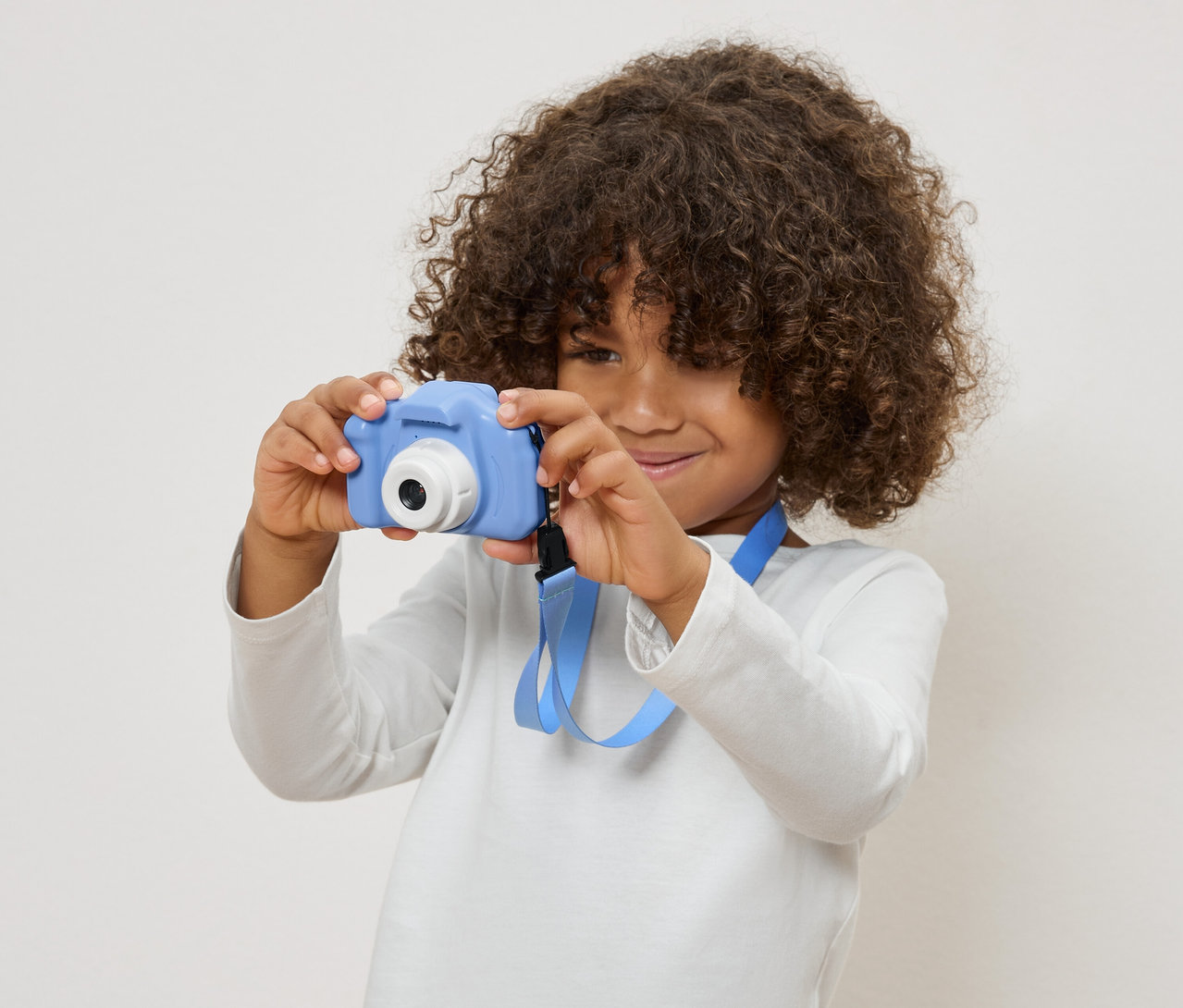 Dziecko z kręconymi włosami trzyma niebieski aparat zabawkowy.