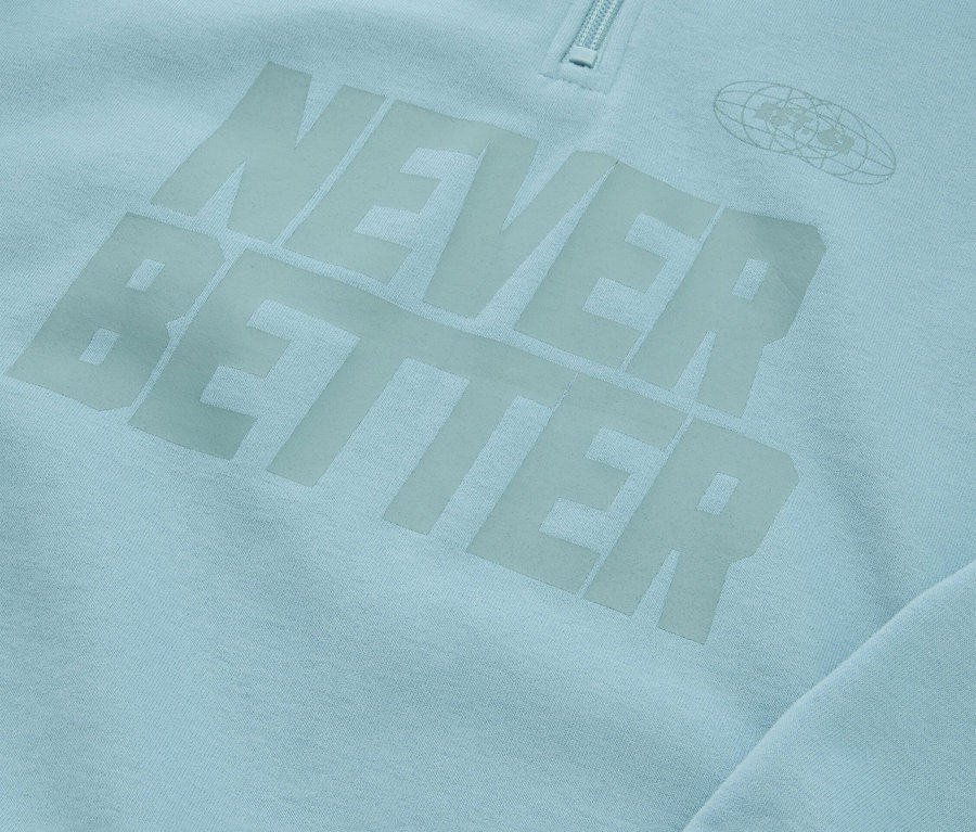 Zbliżenie jasnoniebieskiej bluzy z napisem "NEVER BETTER" i zamkiem błyskawicznym przy kołnierzu.