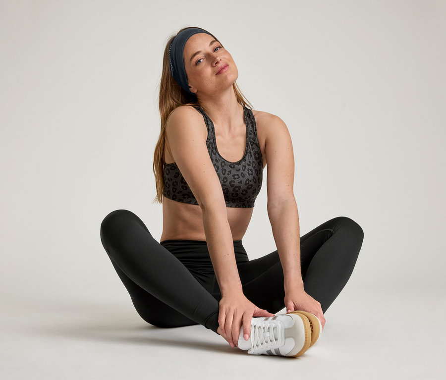 Kobieta siedzi w rozkroku, ma na sobie legginsy sportowe „ActiveSoft”.