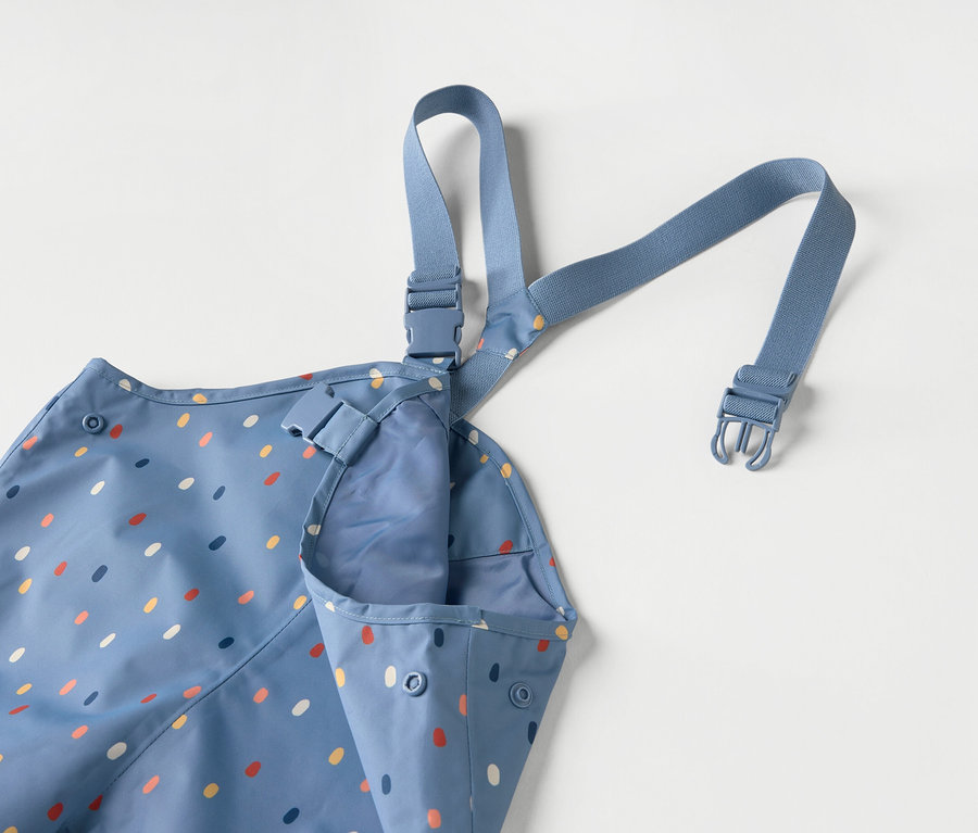 Niebieski fartuch dziecięcy w kolorowe kropki z niebieskimi ramiączkami na białym tle.
