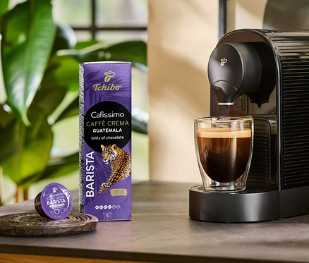 Ekspres przygotowuje kawę Cafissimo BARISTA Caffè Crema Guatemala do szklanki. Obok stoi opakowanie 10 kapsułek i jedna kapsułka.