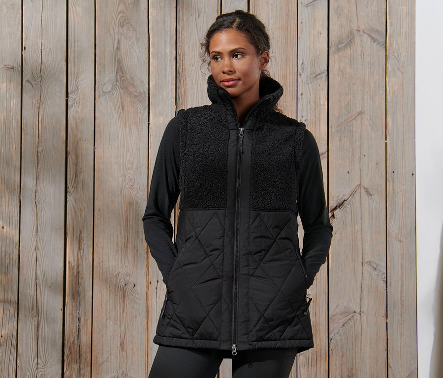 Kobieta ma na sobie czarną pluszową kamizelkę pikowaną.