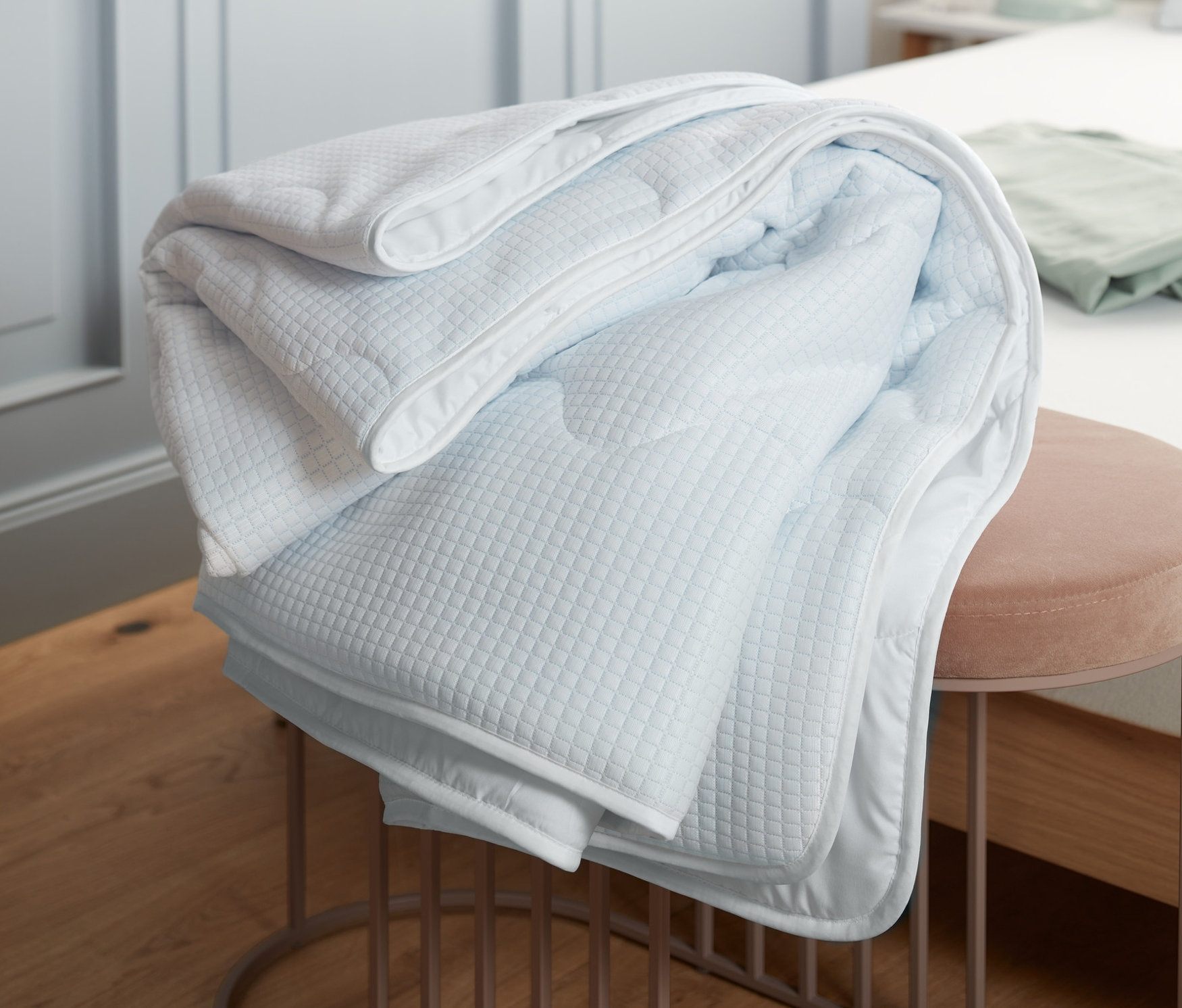 Złożona kołdra chłodząca leży na różowym stołku w sypialni.