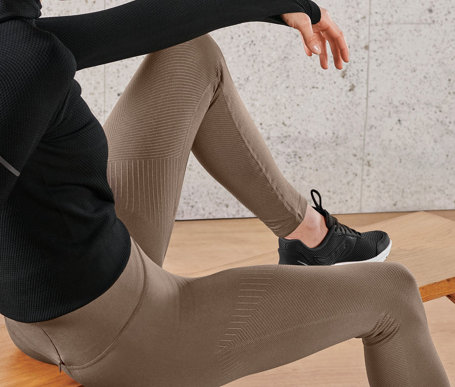 Kobieta siedzi na ławce, ma na sobie bezszwowe legginsy do biegania i czarne tenisówki.