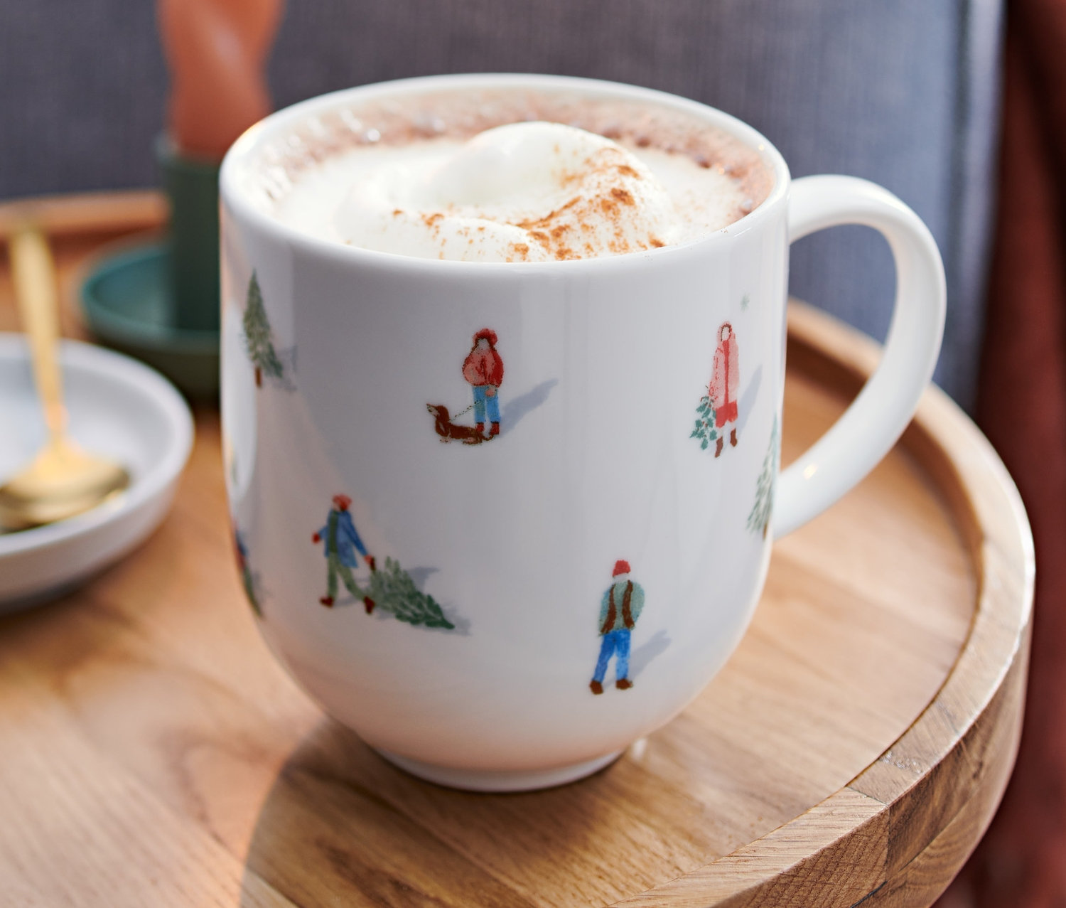 Na drewnianym stoliku stoi duży kubek z gorącym napojem i bitą śmietaną. W tle płonąca świeca i fragment sofy.