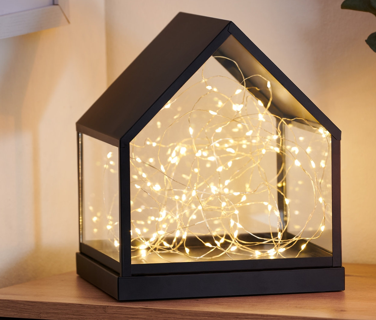 Na drewnianej komodzie stoi szklany domek LED.