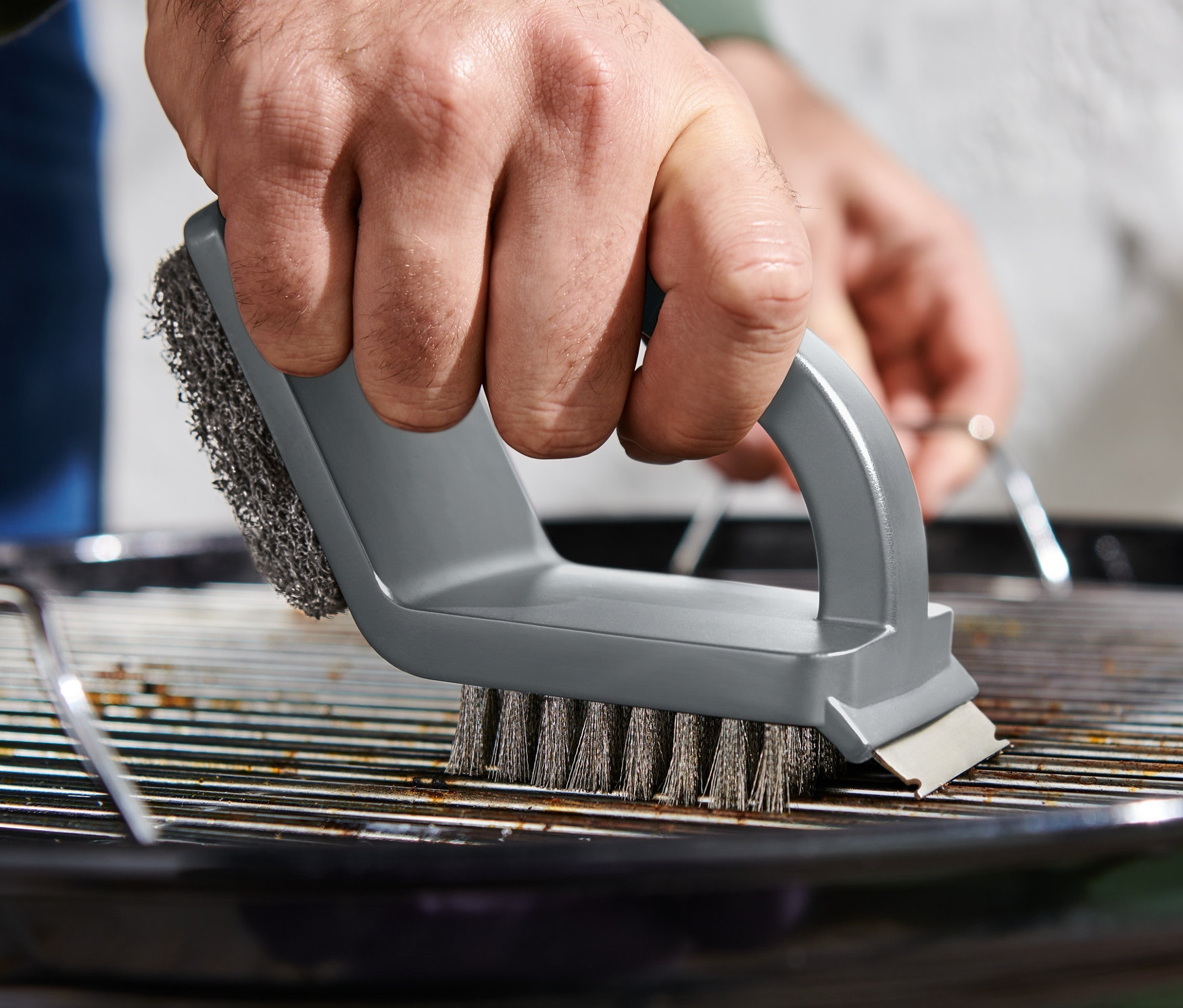 Mężczyzna czyści ruszt grilla szczotką do czyszczenia 3 w 1.