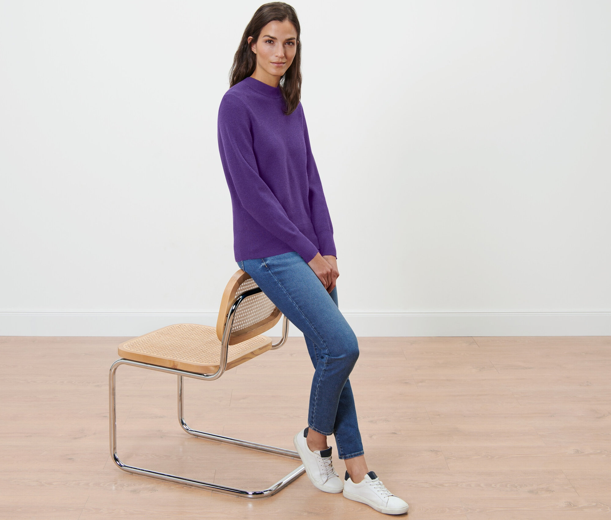 Kobieta siedzi na krześle i ma na sobie fioletowy sweter z delikatnej dzianiny.