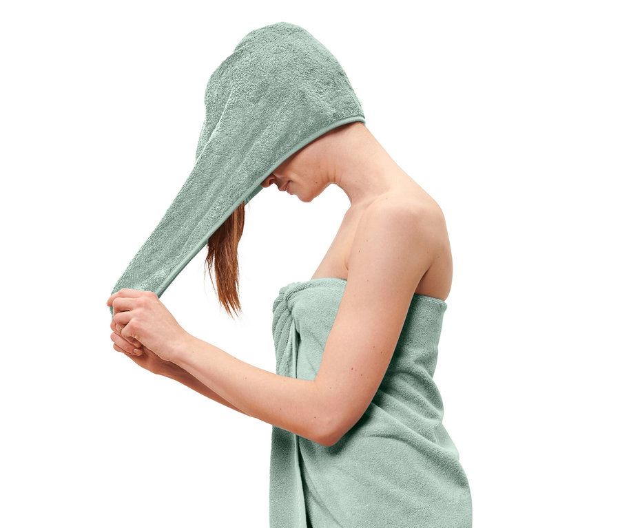 Kobieta zakłada na głowę jasnoniebieski ręcznik turban, a na ciele ma owinięty jasnoniebieski ręcznik.