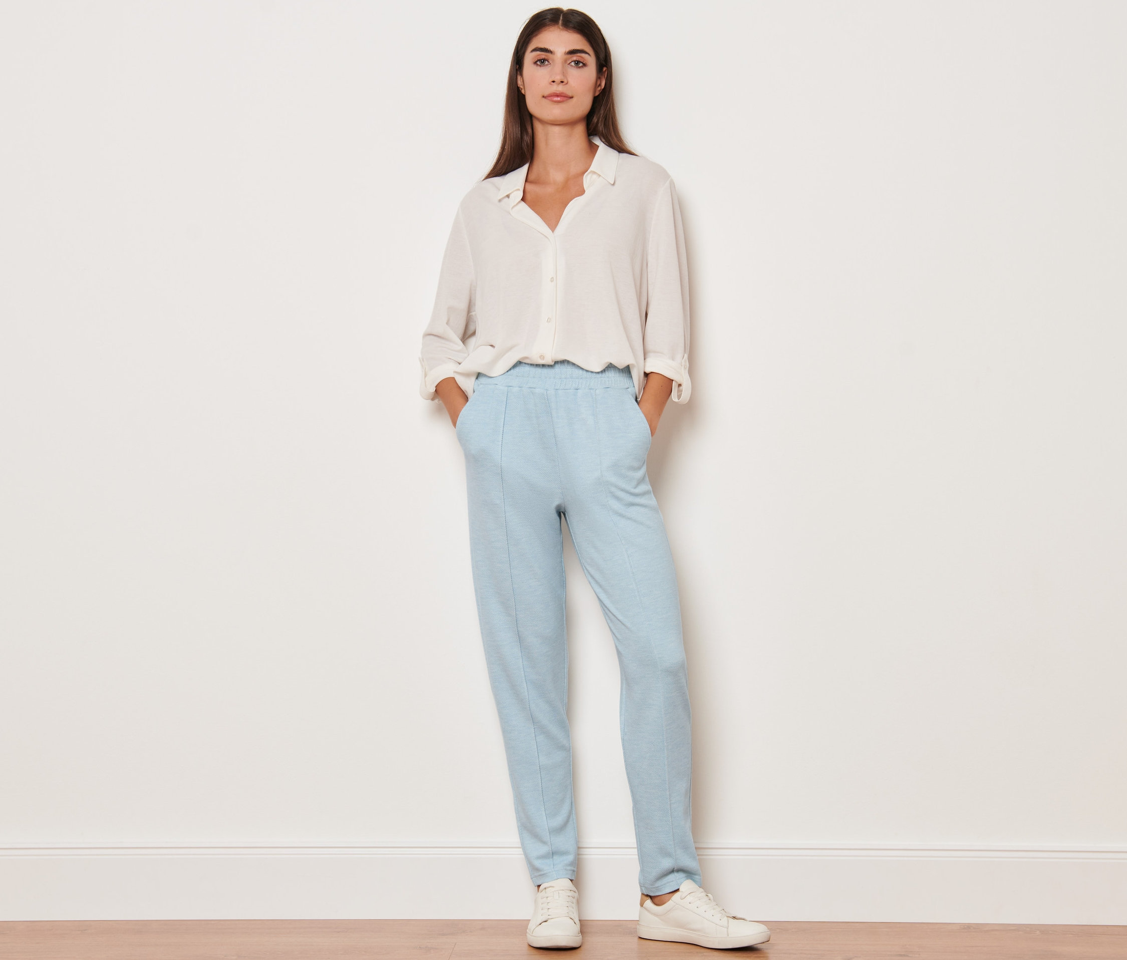 Kobieta stoi z rękami w kieszeniach spodni dresowych z kantem.