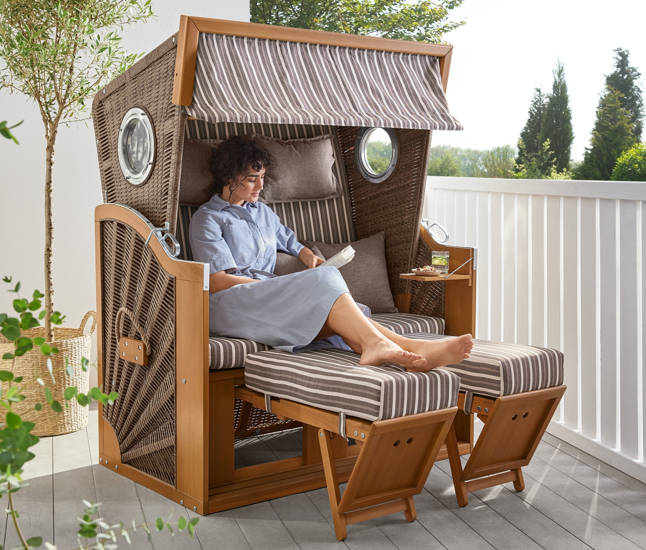 Kobieta siedzi w koszu plażowym premium XL z rozkładanym stolikiem i czyta.
