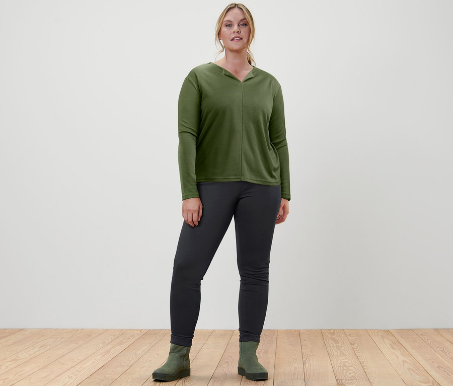 Kobieta stoi i ma na sobie bluzkę, jegginsy i botki ze skóry zamszowej.