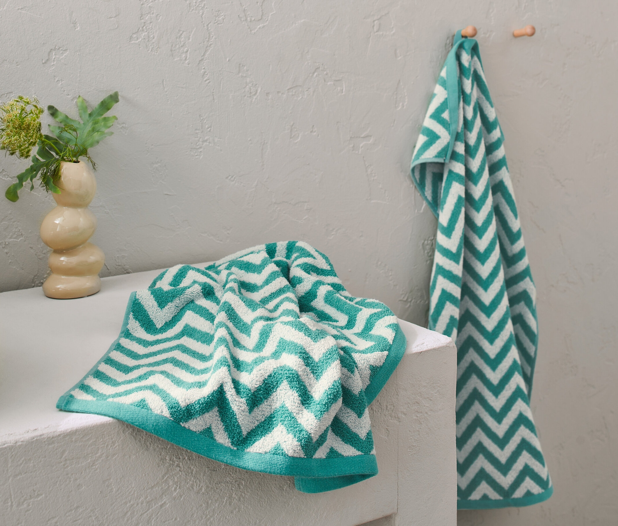 Dwa ręczniki żakardowe w kolorze morskim leżą na umywalce, jeden wisi na haczyku.