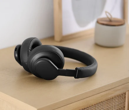 Czarne słuchawki Bluetooth® z funkcją dotykową leżą na jasnym drewnianym stole.