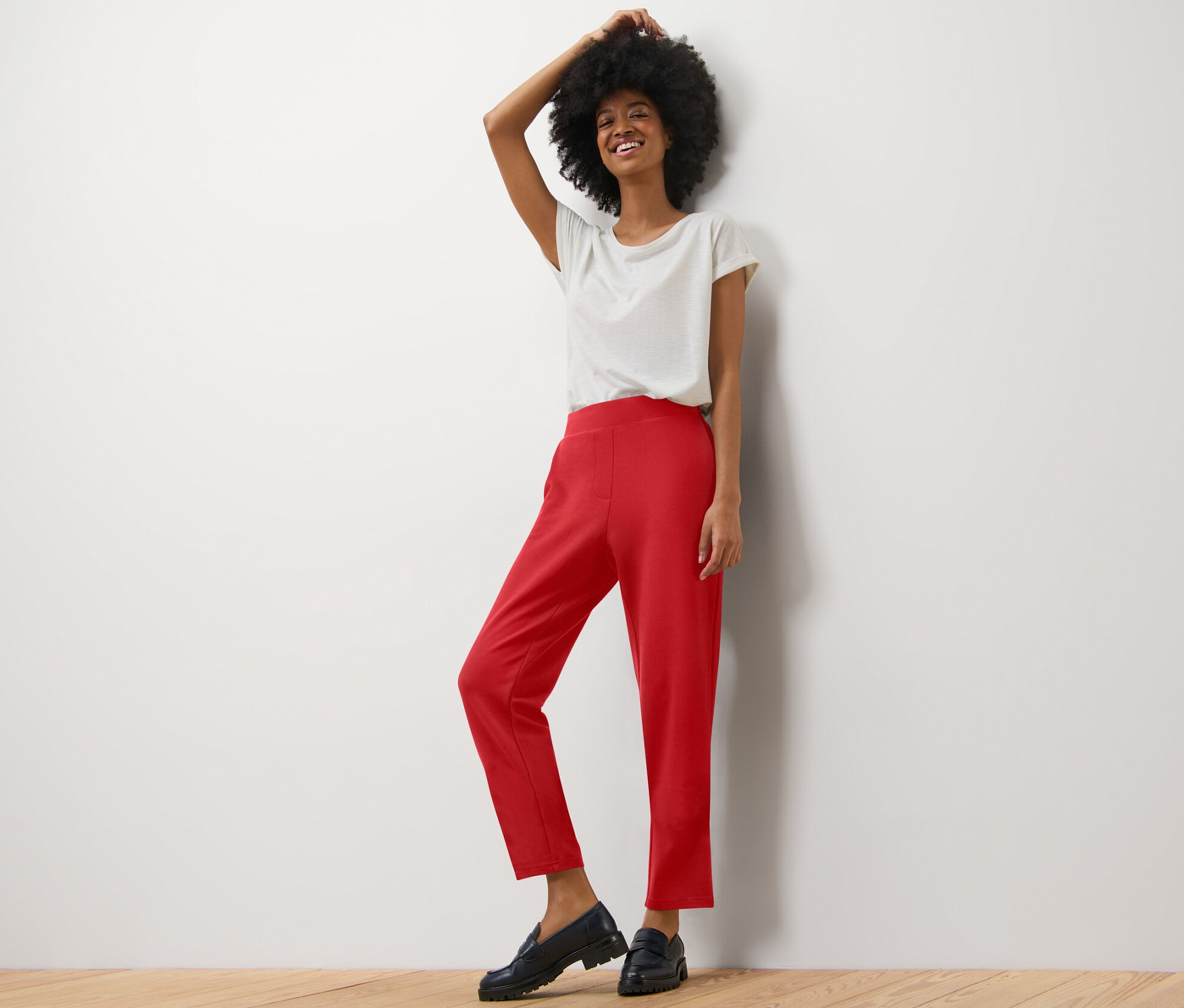 Kobieta pozuje w jasnej koszulce i czerwonych spodniach dresowych.