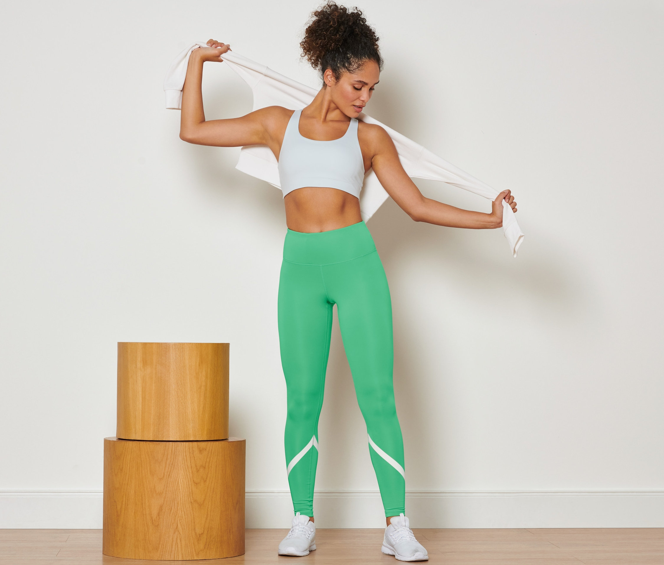 Kobieta zarzuca ręcznik na ramiona, ubrana w zielone legginsy sportowe.