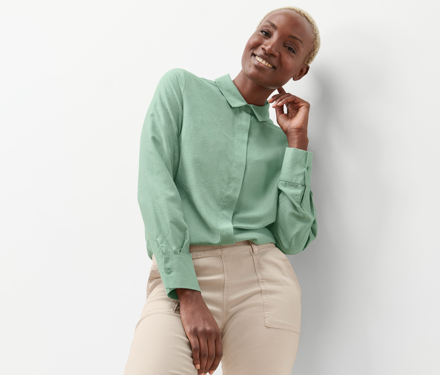 Uśmiechnięta kobieta pozuje w zielonej bluzce żakardowej.