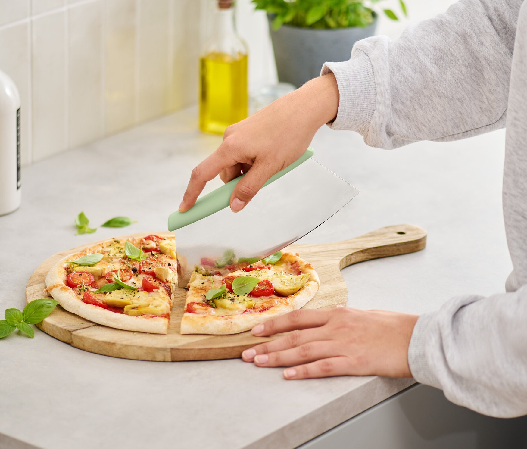 Kobieta kroi pizzę na drewnianej desce za pomocą krajalnicy do pizzy i ziół.