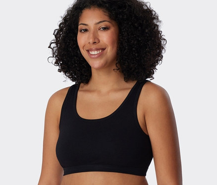 Kobieta z kręconymi włosami ma na sobie czarną braletkę z bawełny ekologicznej SCHIESSER, 2 sztuki.